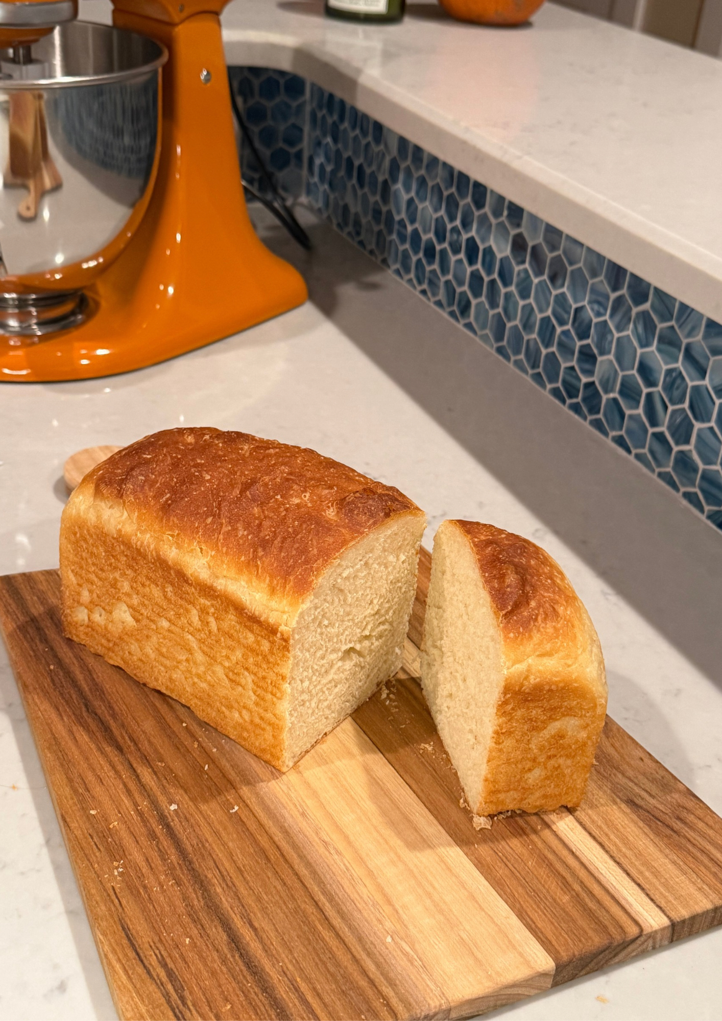 A loaf bread with in the background some vegetables and freshly baked bagels.
