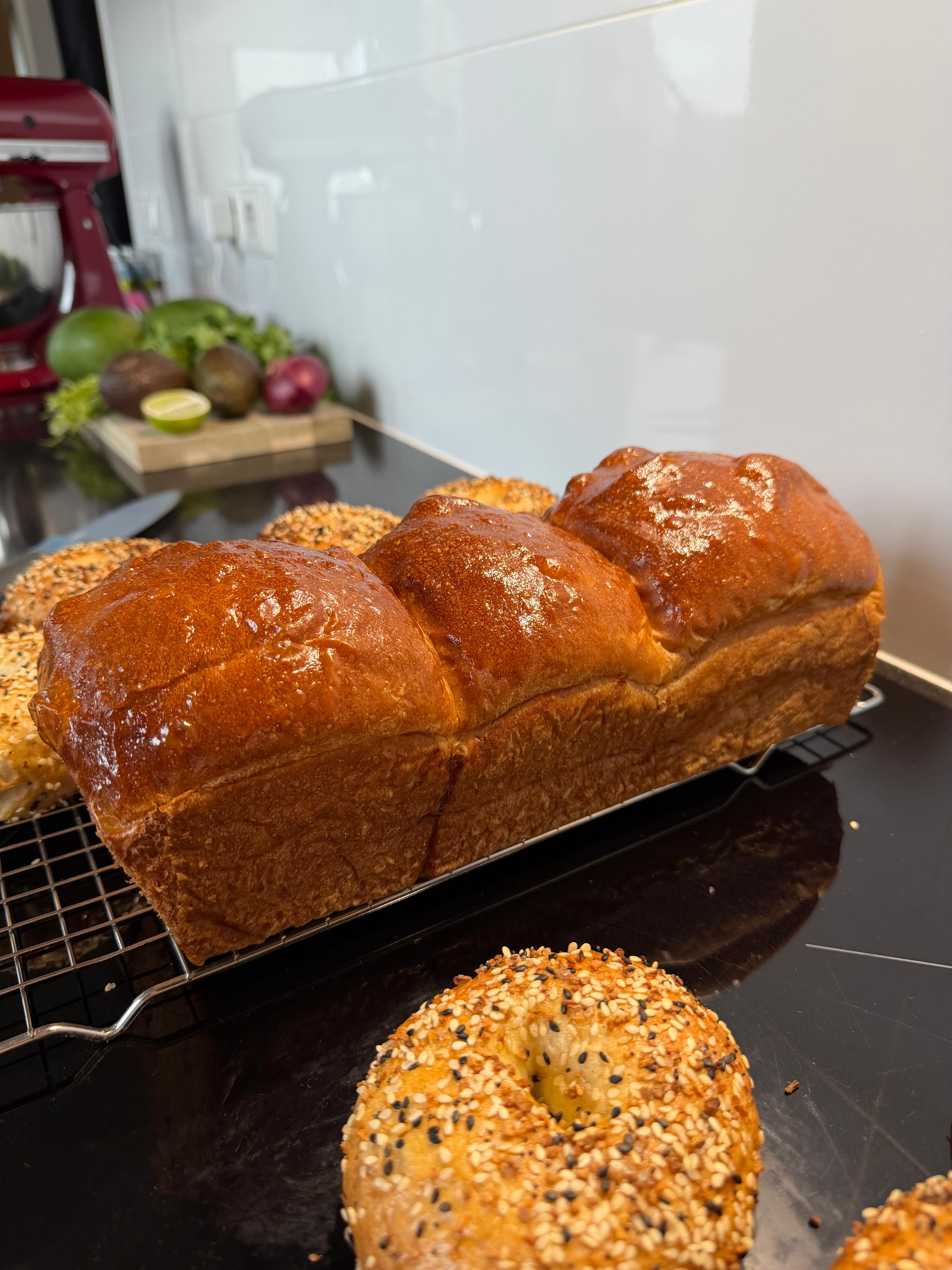A loaf bread with in the background some vegetables and freshly baked bagels