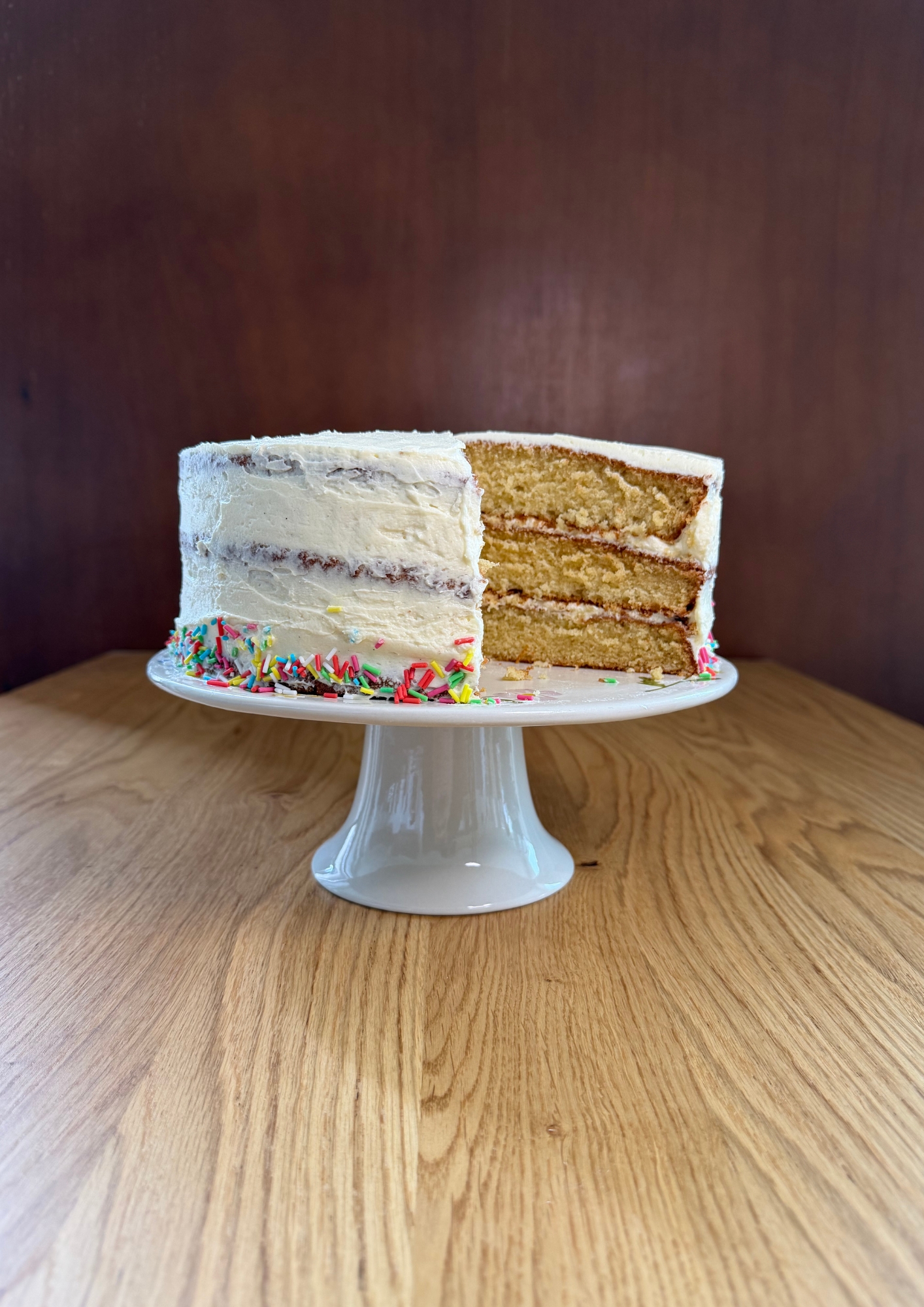 A three-tier vanilla cake with an ermine frosting and some funfetti sprinkles around the base